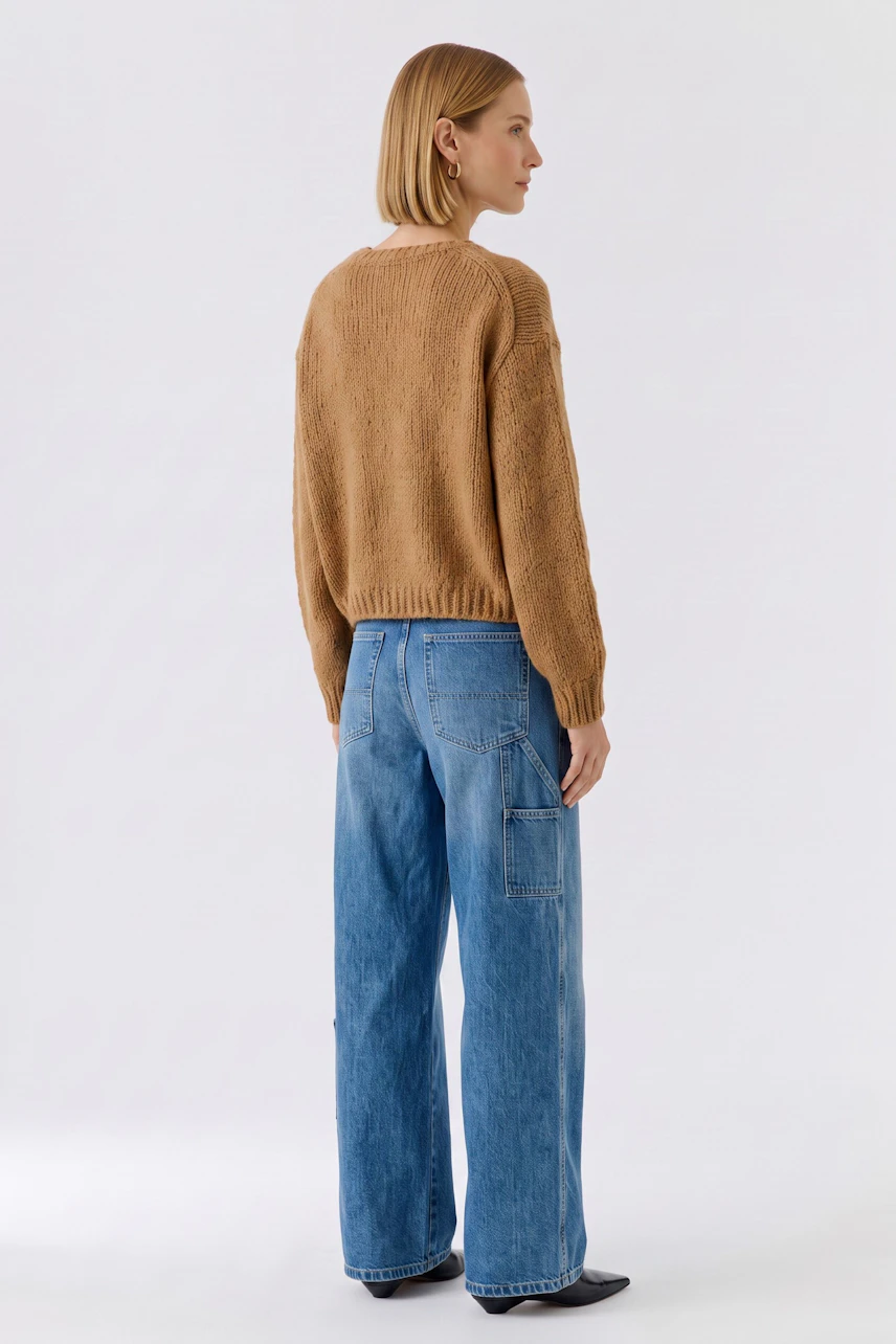 Lässiger Damen-Pullover: Frau im beigen Strickpullover und blauen Jeans von hinten betrachtet.