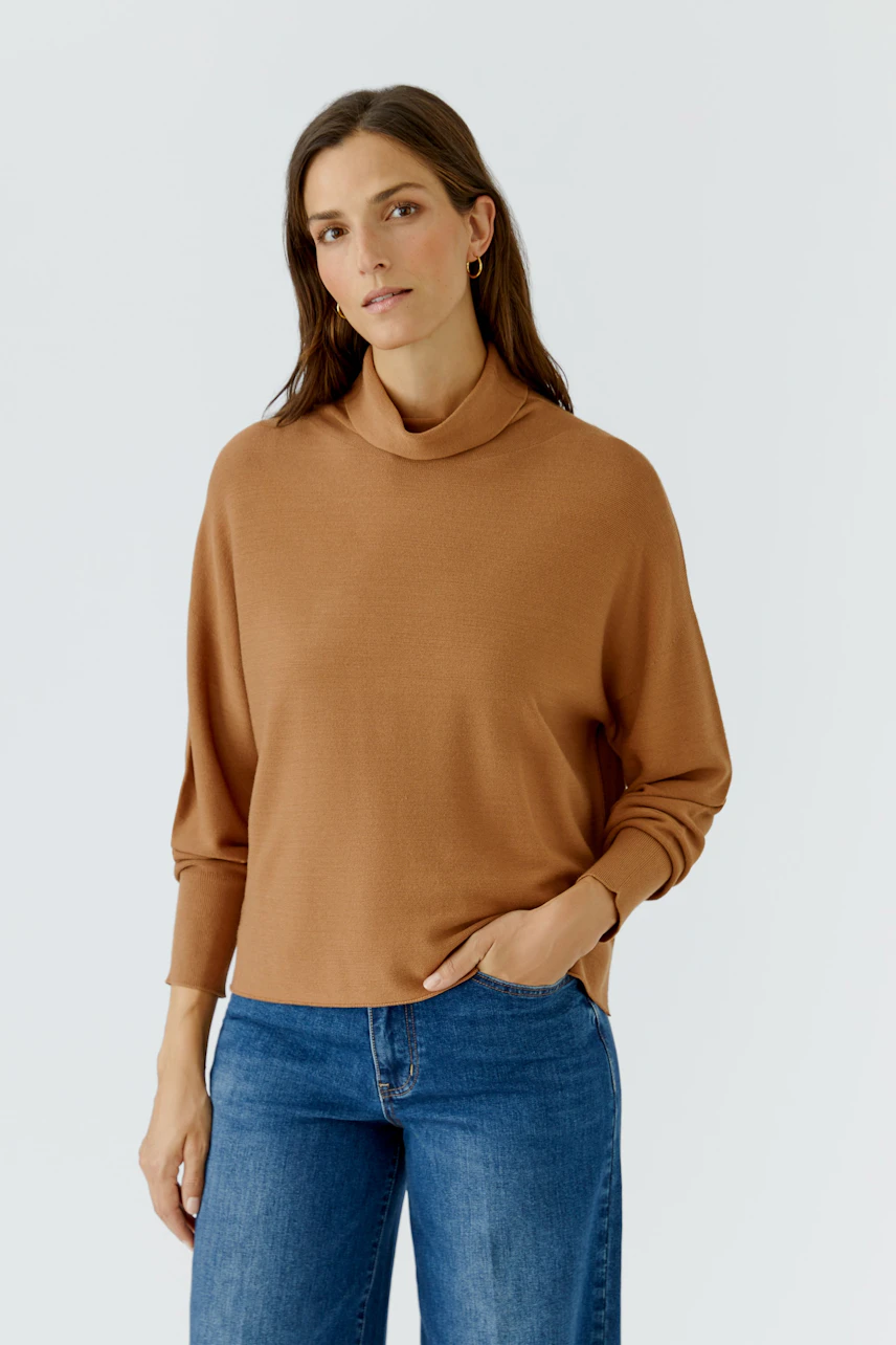 Casual women's pullover: Woman in a brown pullover with relaxed fit and blue jeans, exuding a calm presence.