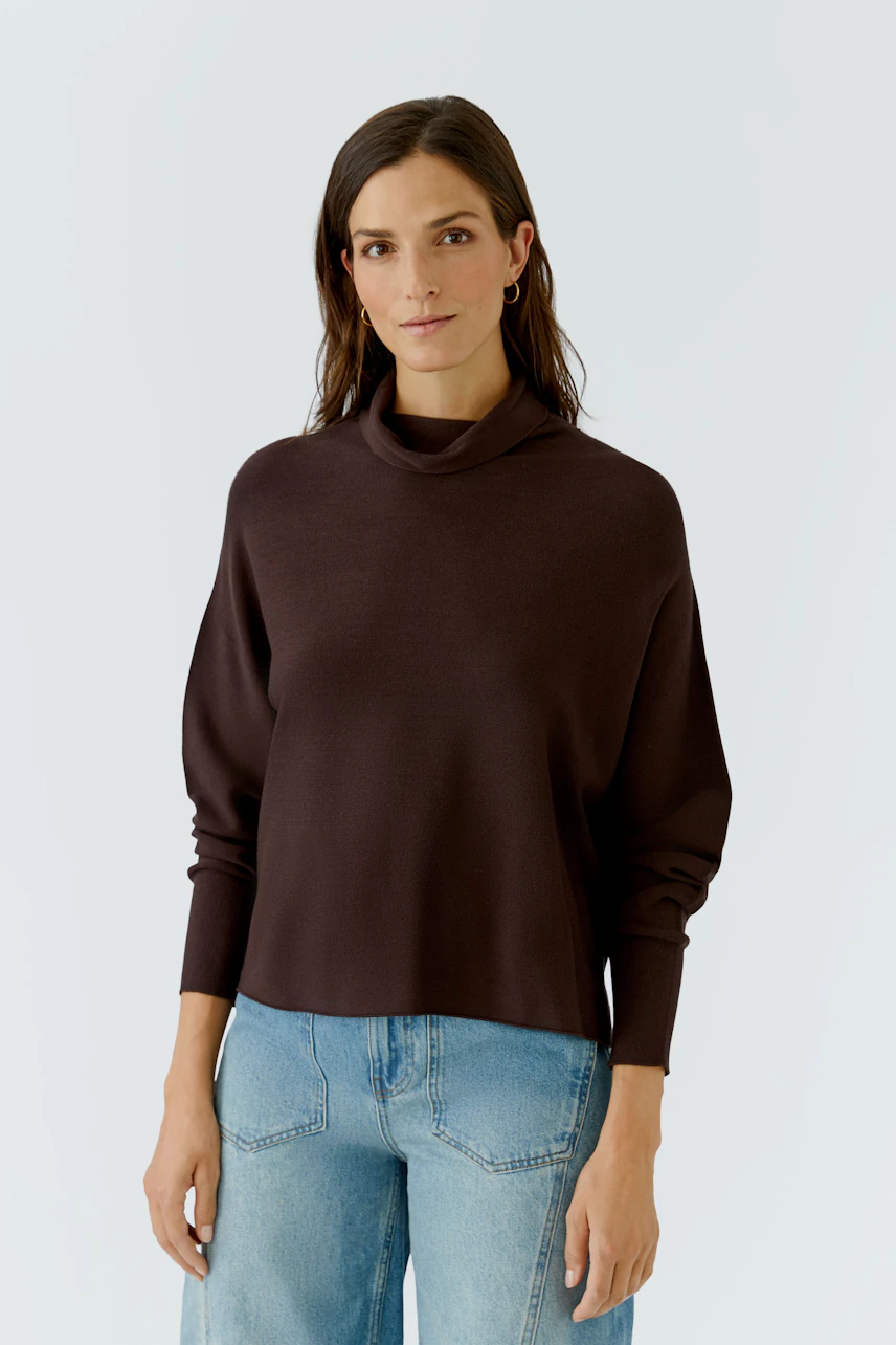 Casual women's pullover: Woman in a brown pullover with relaxed fit and light blue jeans, looking composed.