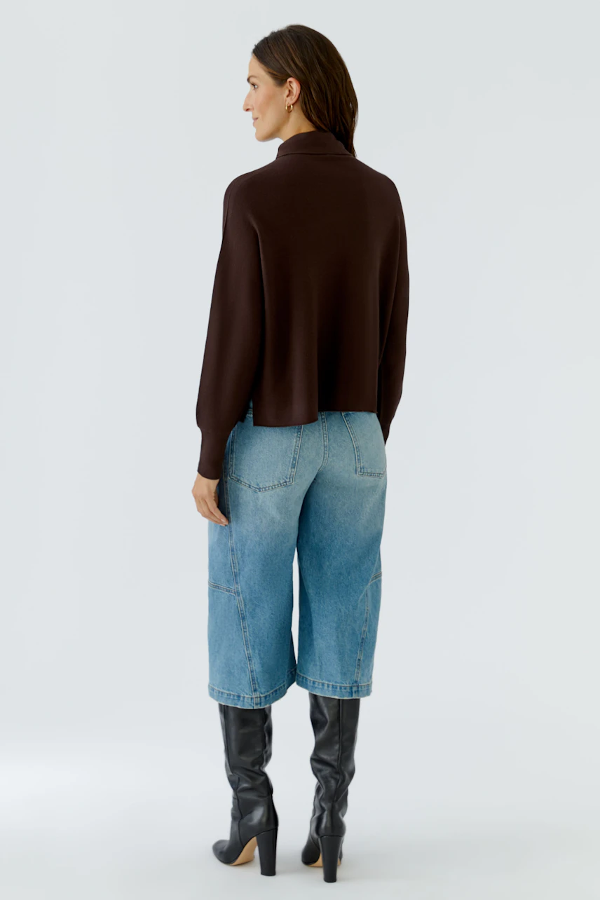 Casual pullover: Woman in brown pullover, blue jeans, and black boots, viewed from the back.