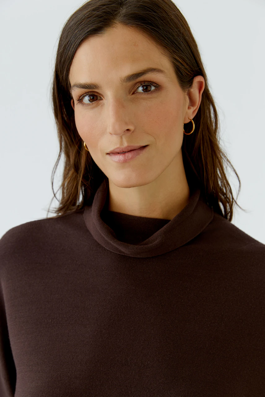 Woman in a brown pullover with a relaxed fit, featuring a subtle cowl neck, looking confidently at the camera.