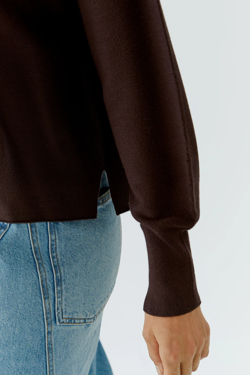 Casual pullover: Woman in a dark pullover with relaxed fit, paired with blue jeans, showcasing side detail.
