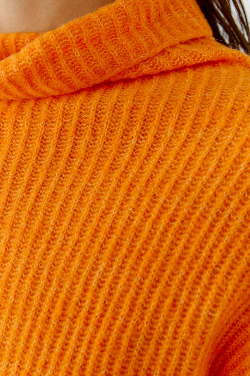 Strukturierter Damen-Pullover: Frau im leuchtend orangefarbenen Strickpullover mit Kapuze.