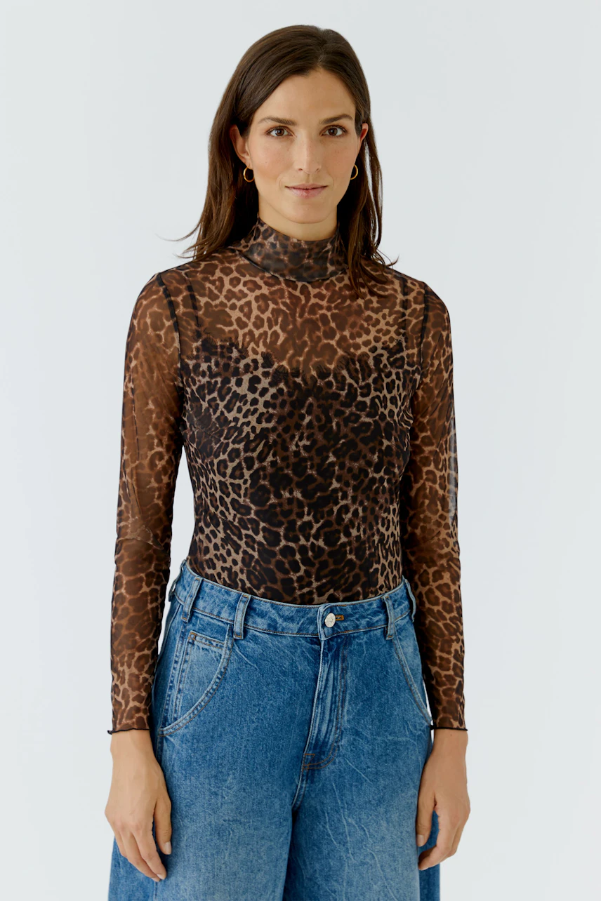 Woman in leopard print long-sleeve shirt and blue jeans, standing confidently.