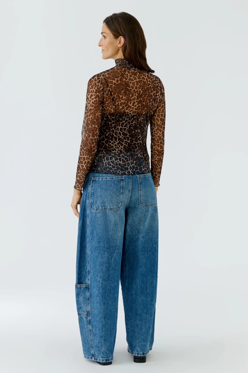 Woman in leopard print long-sleeve shirt and wide blue jeans, viewed from the back.