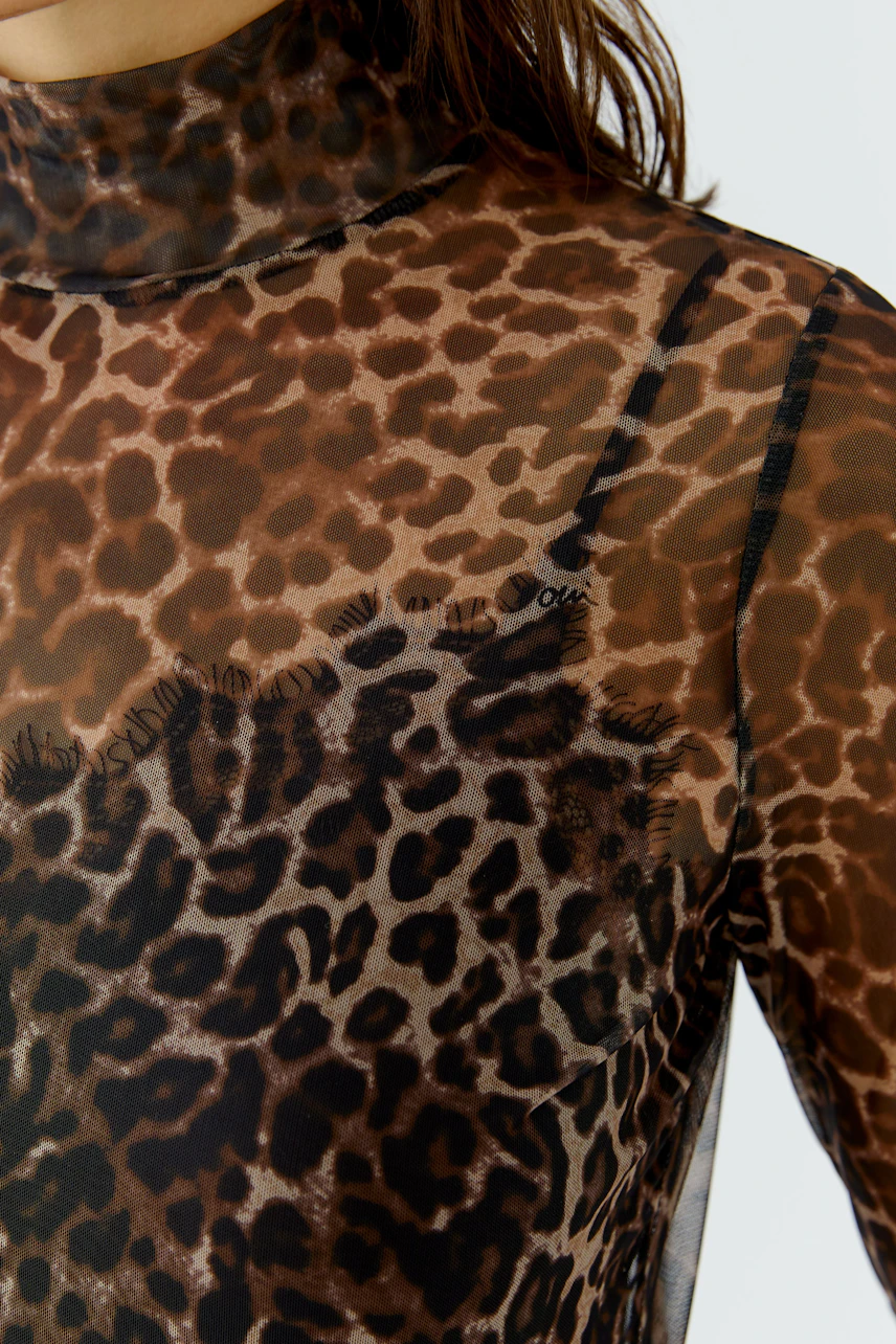 Women's long-sleeve shirt: Sheer leopard print with high neck, worn by a woman, showcasing bold style.