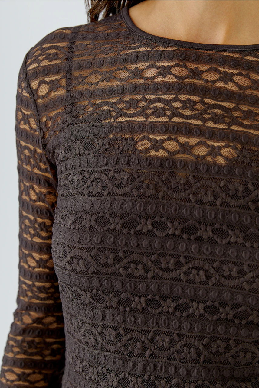 Damen-Langarmshirt: Frau trägt ein schwarzes, durchbrochenes Shirt mit feinem Muster.