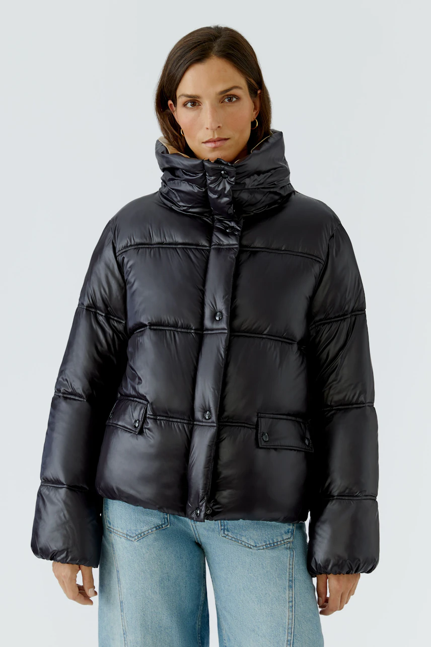 Damen-Outdoorjacke: Frau in schwarzer, gesteppter Jacke mit hohem Kragen und blauer Jeans.