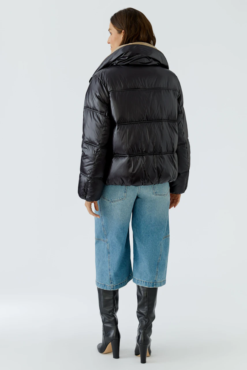 Schwarze Outdoorjacke: Frau in gesteppter Jacke, kombiniert mit Jeans und Stiefeln, von hinten zu sehen.