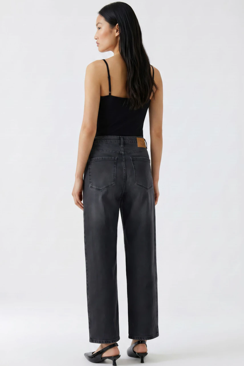 Jeans Barrel: Frau in schwarzem Top und lässiger, dunkler Barrel-Jeans von hinten.