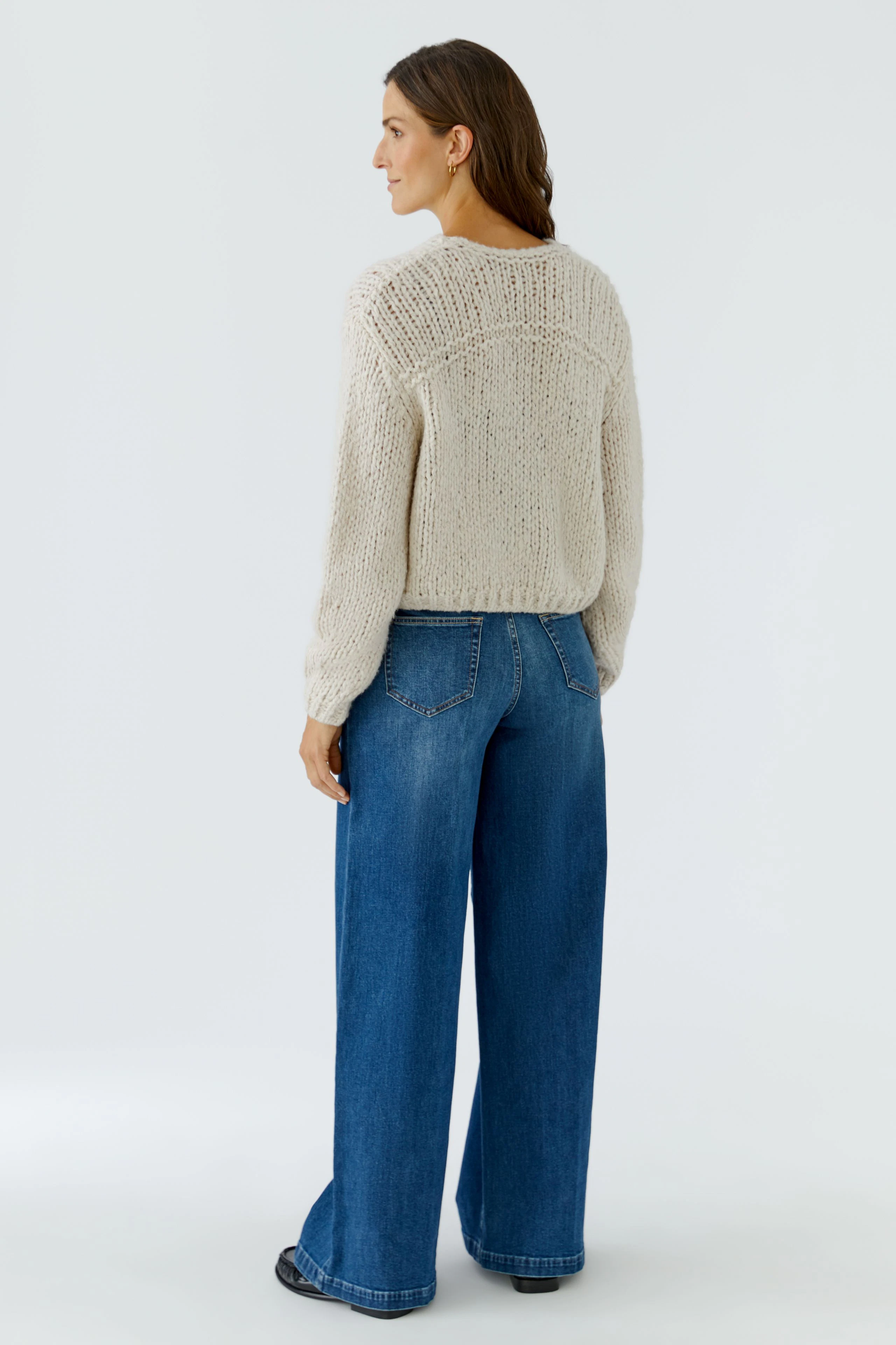 Casual knit cardigan: Woman in beige cardigan and wide-leg jeans, viewed from the back.