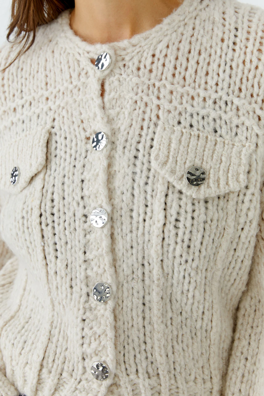 Cozy knit cardigan: Woman in cream button-up cardigan with textured pattern and metallic buttons.