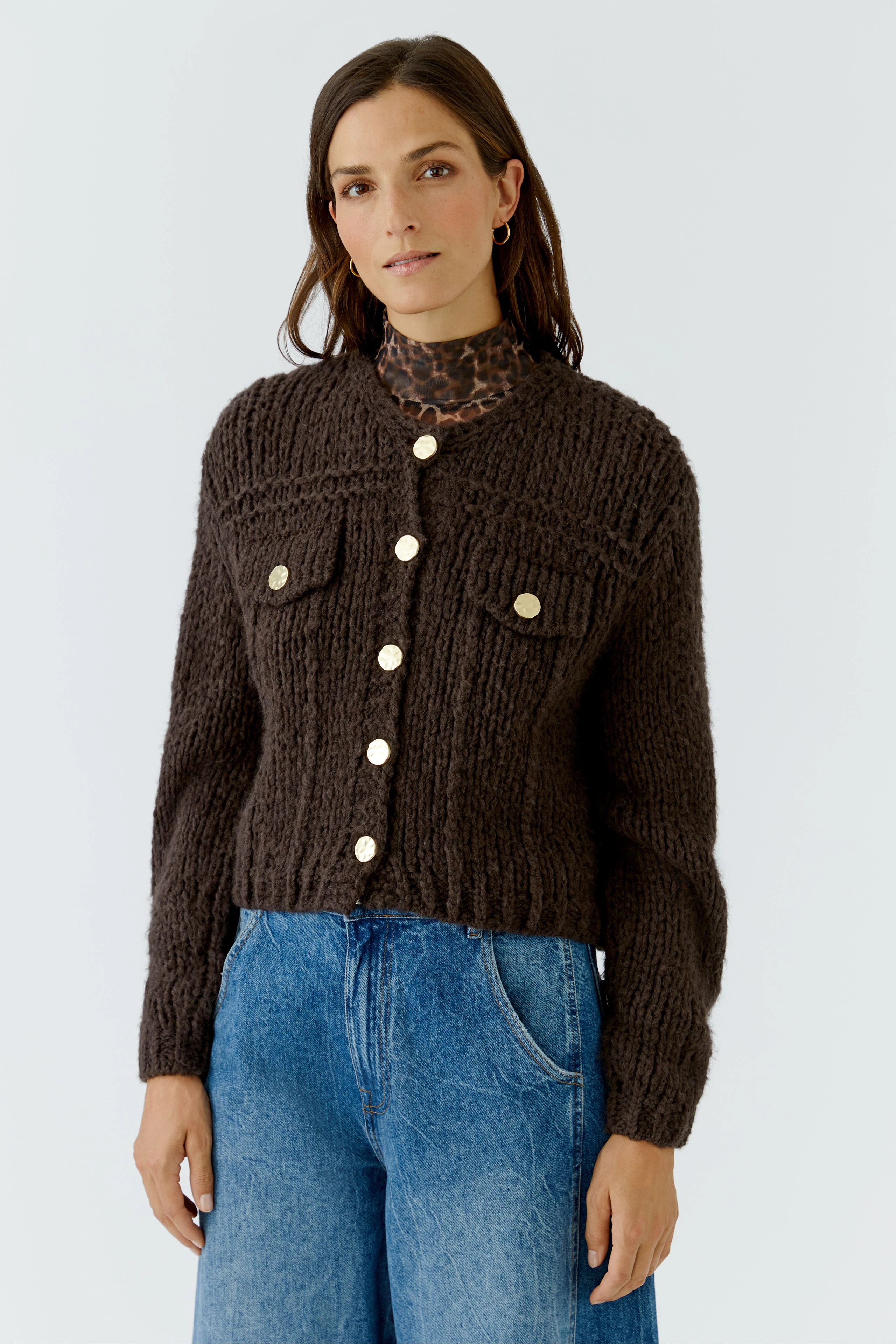 Woman in chunky knit cardigan with gold buttons, paired with blue jeans and leopard print top.