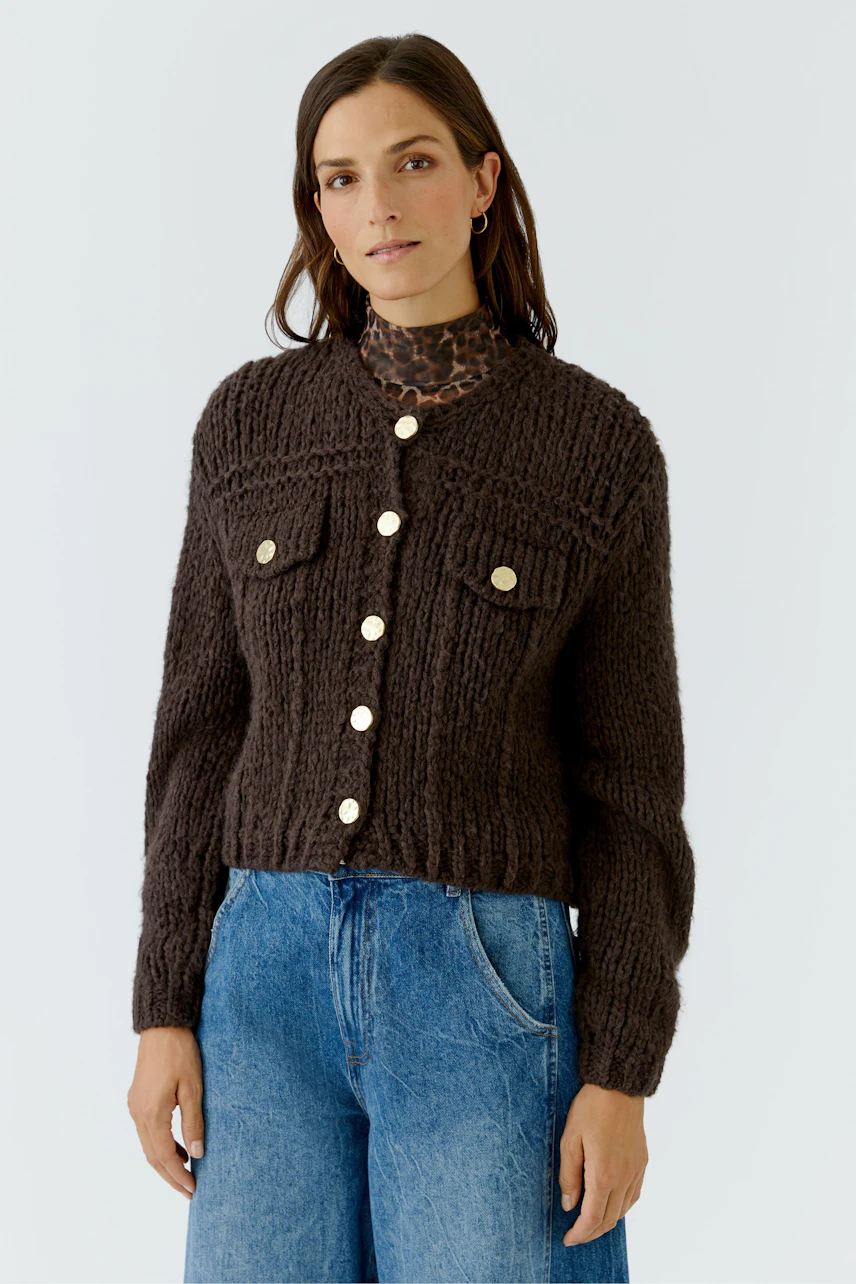 Woman in chunky knit cardigan with gold buttons, paired with blue jeans and leopard print top.
