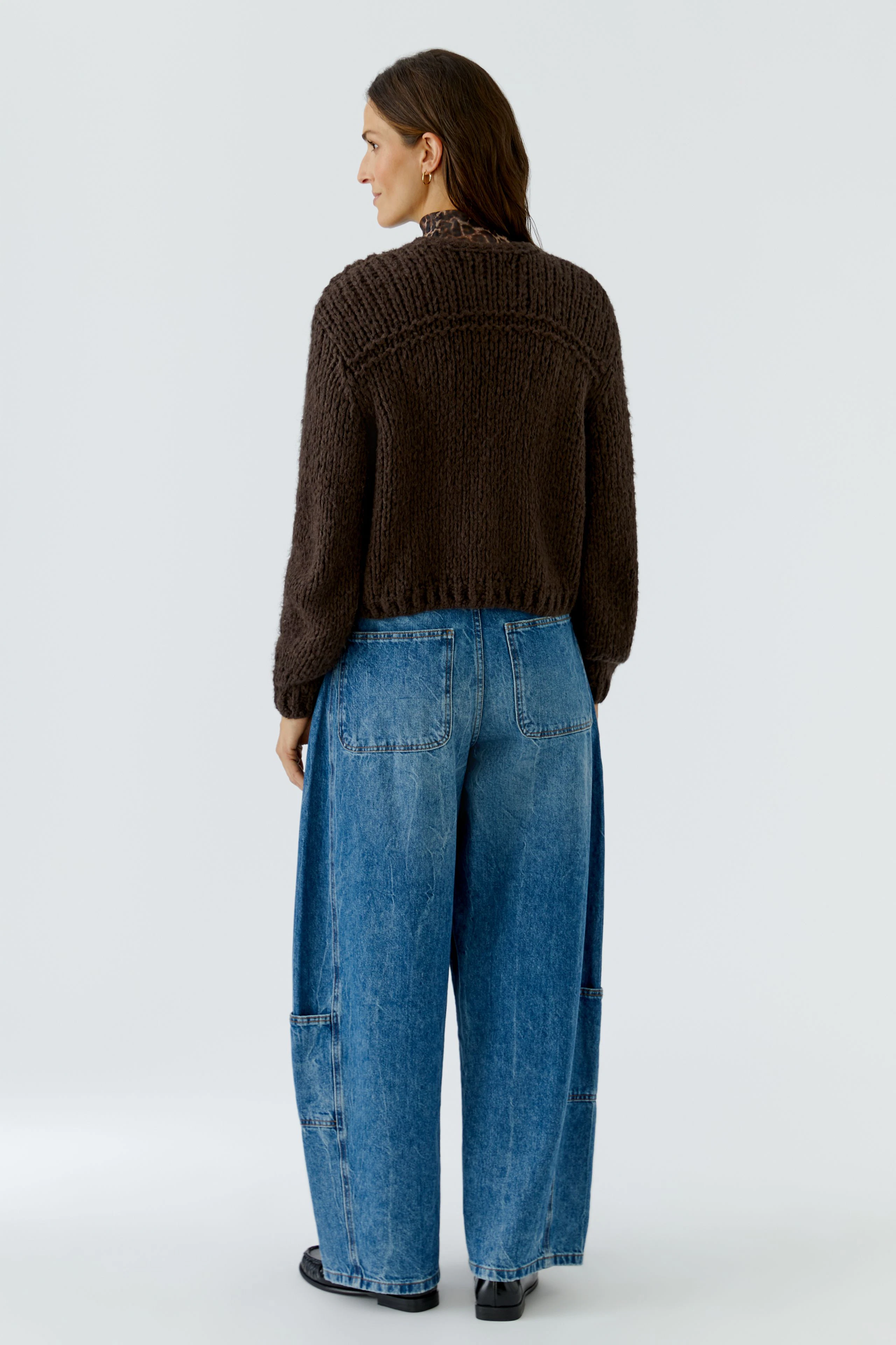 Casual cardigan: Woman in a brown knit cardigan and wide blue jeans, viewed from the back.