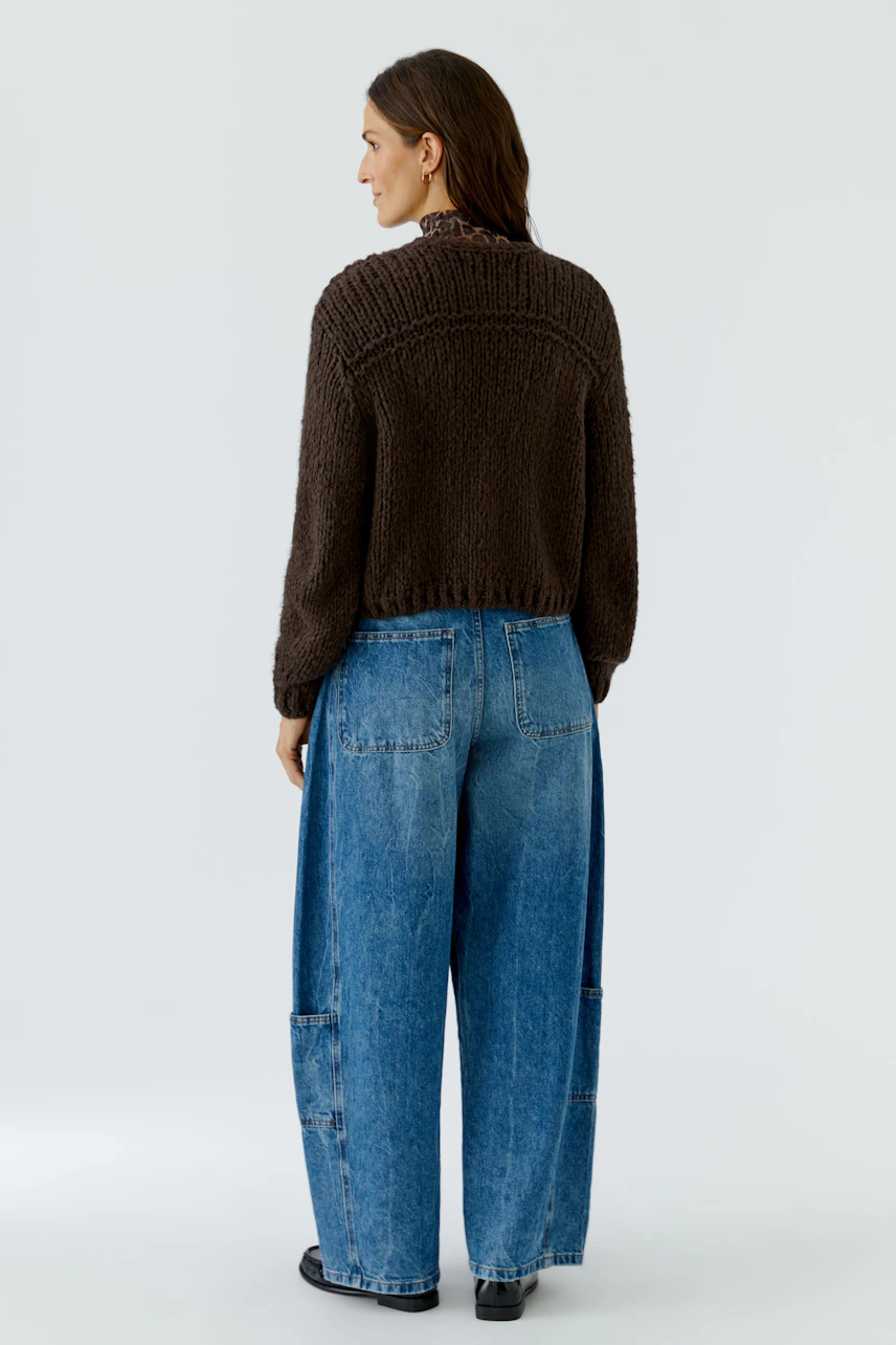 Casual cardigan: Woman in a brown knit cardigan and wide blue jeans, viewed from the back.
