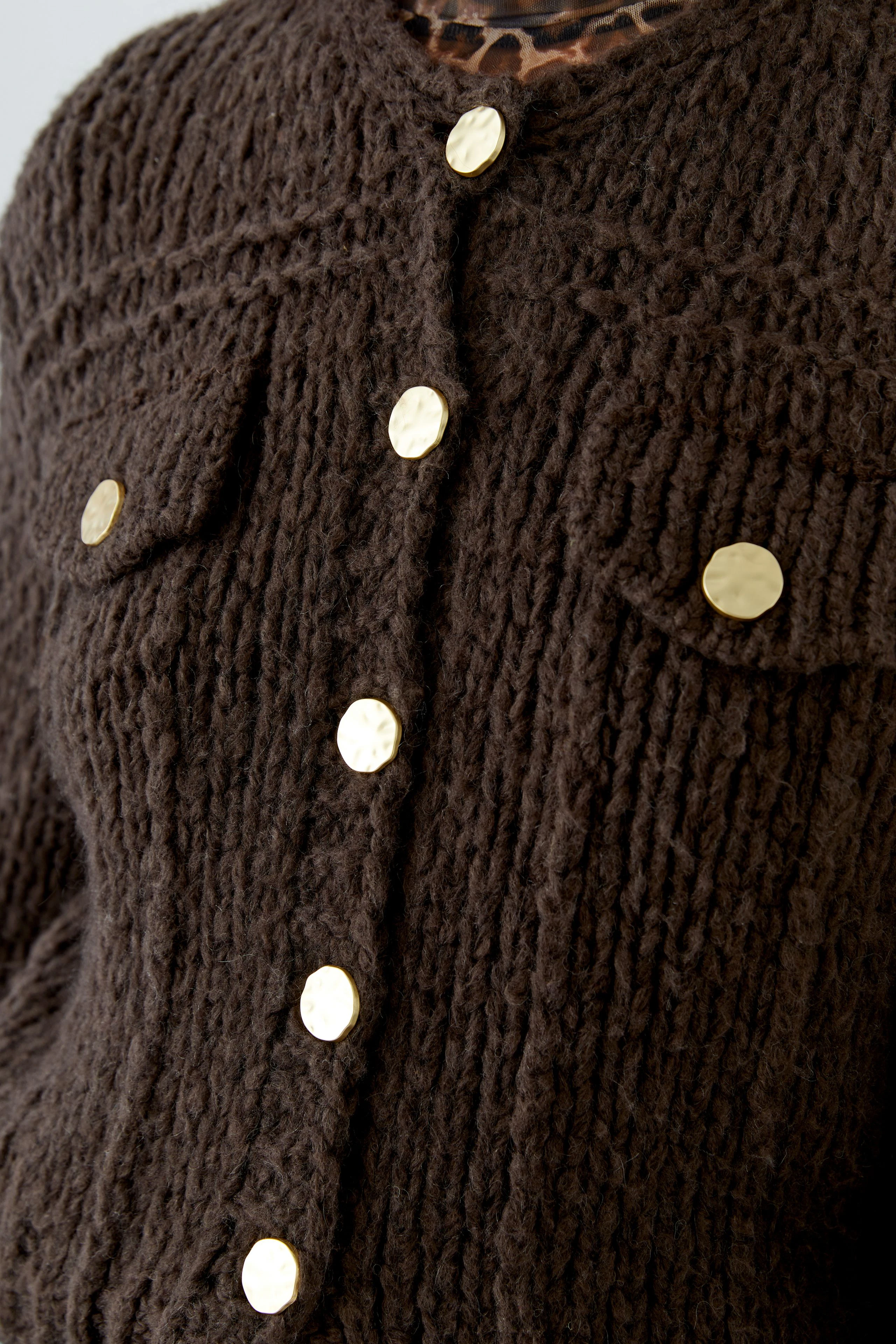 Chunky knit cardigan with gold buttons, close-up of textured fabric. No model visible.