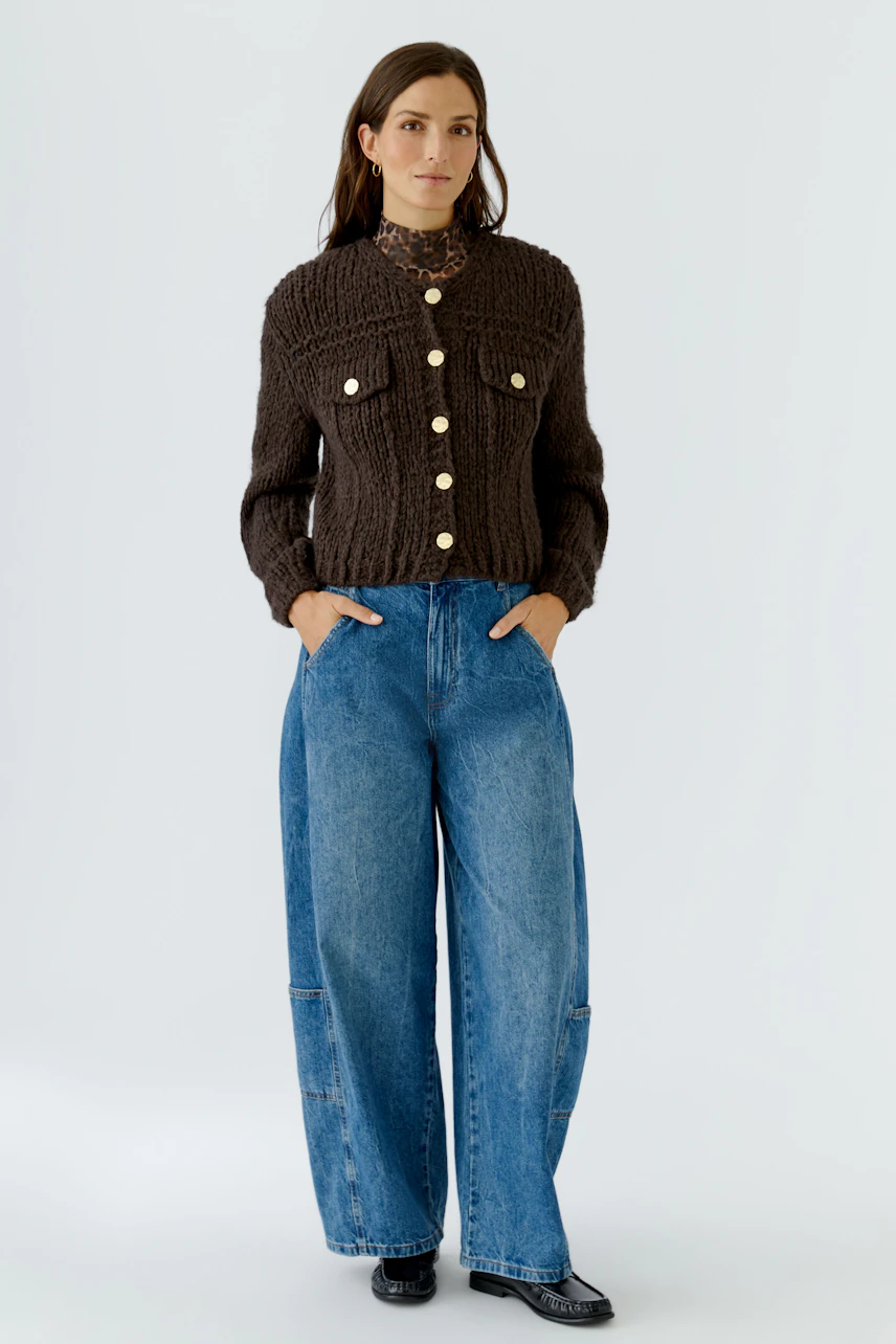 Woman in a chunky knit cardigan with large buttons, paired with wide-leg jeans, standing confidently.