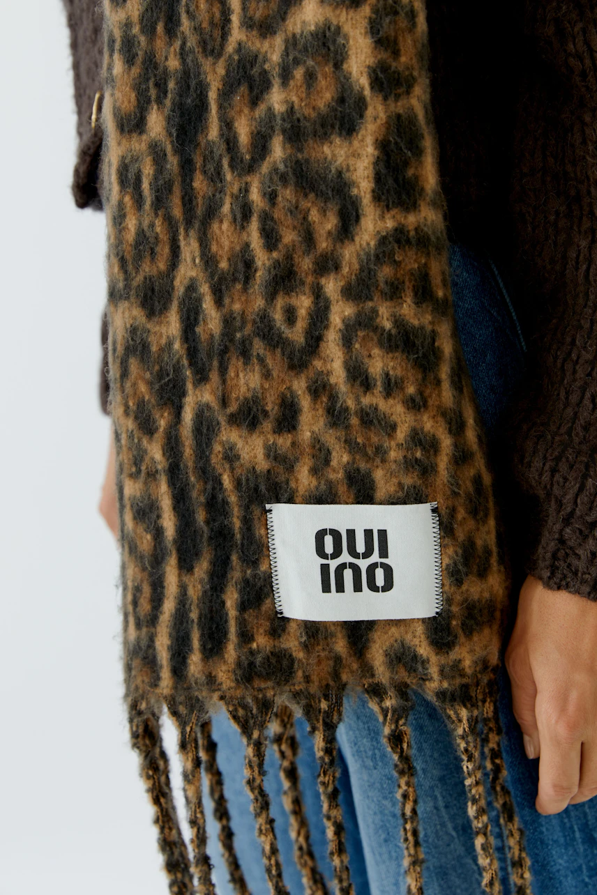 Leopard print scarf: Woman in a cozy brown sweater and jeans, showcasing a stylish fringed scarf.