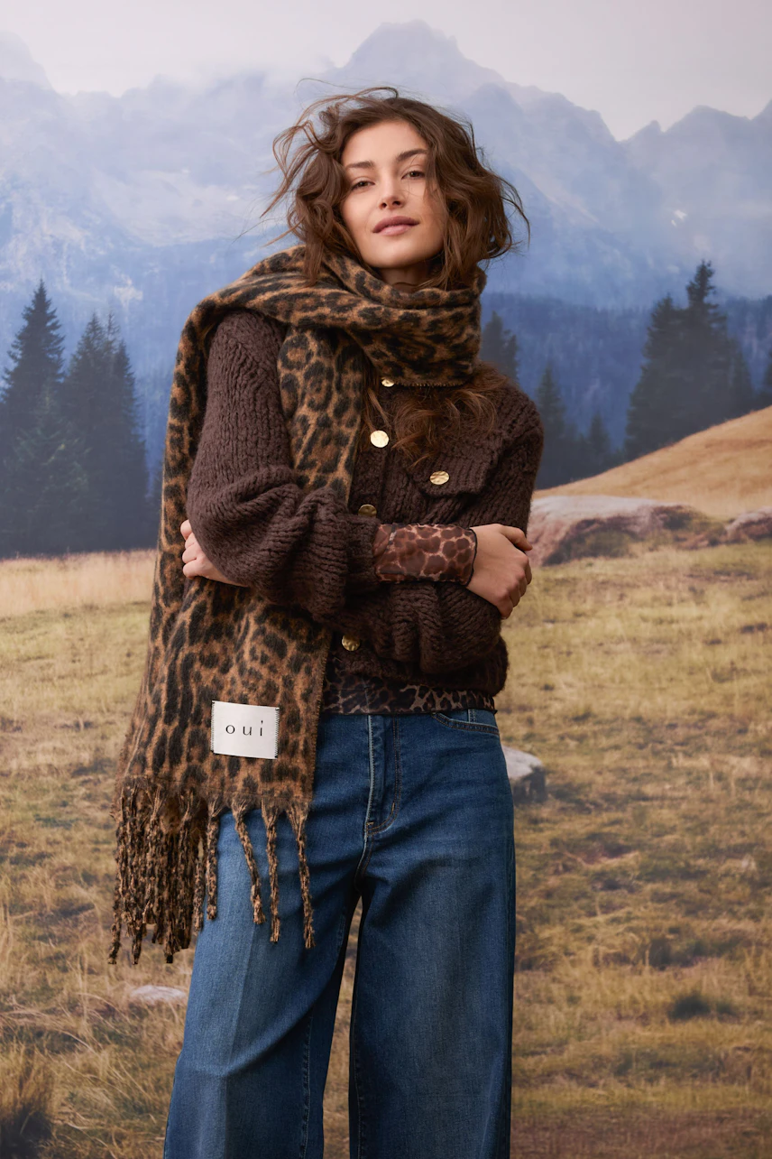 Woman in a cozy leopard print scarf, brown knit pullover, and jeans, standing confidently outdoors.