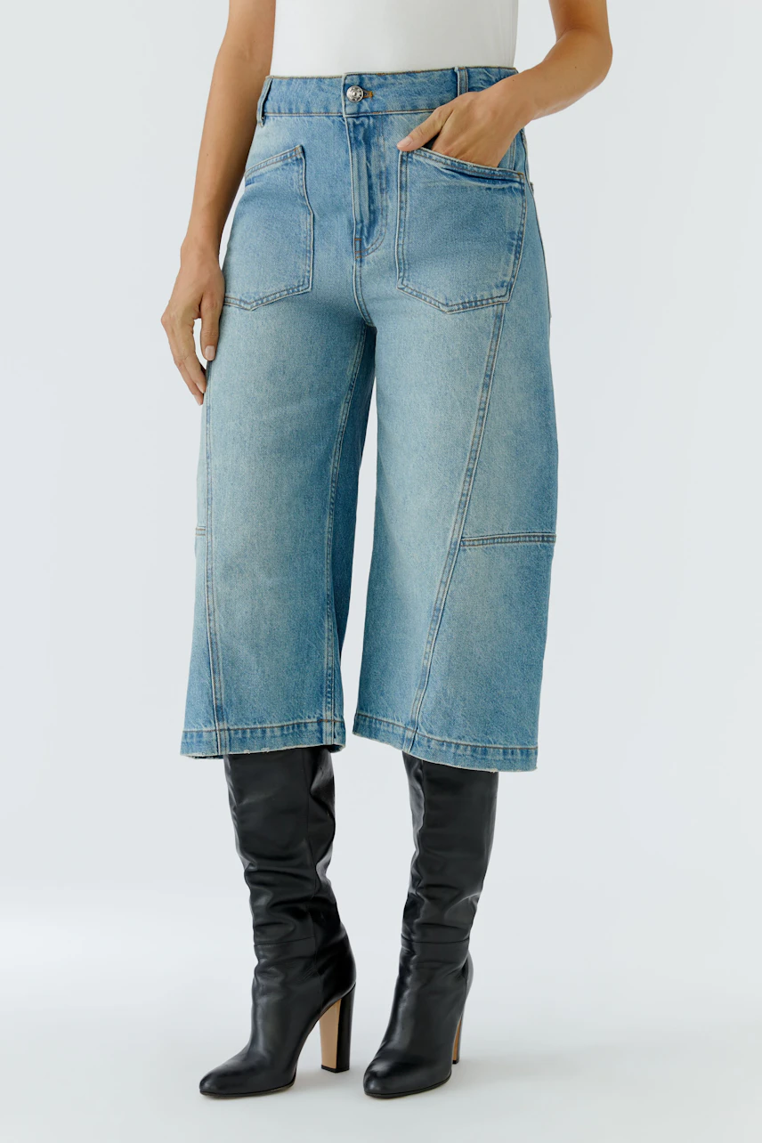 Damen-Culotte: Frau in blauer Jeans-Culotte mit hohen schwarzen Stiefeln, lässig und modern.