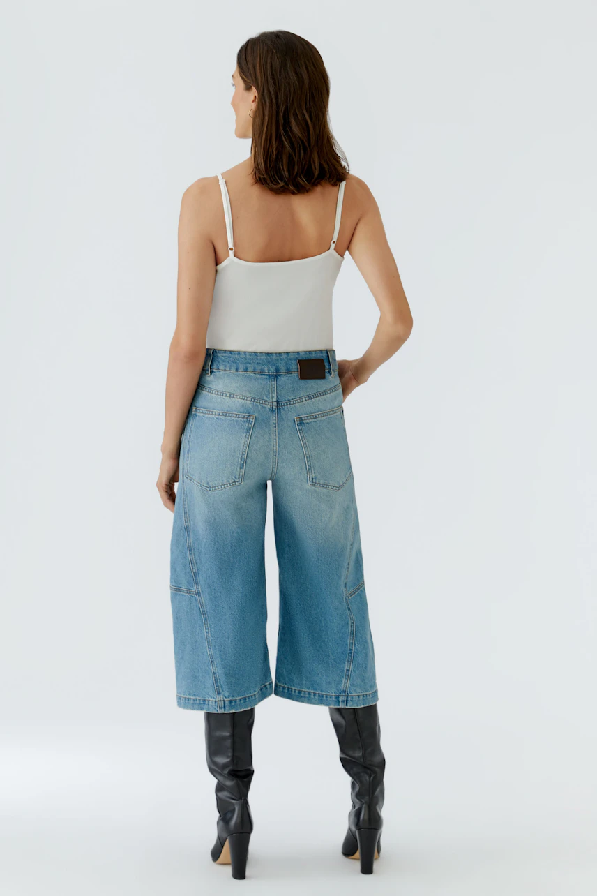 Frau in blauer Jeans-Culotte, weißem Top und schwarzen Stiefeln. Rückansicht des lässigen Outfits.