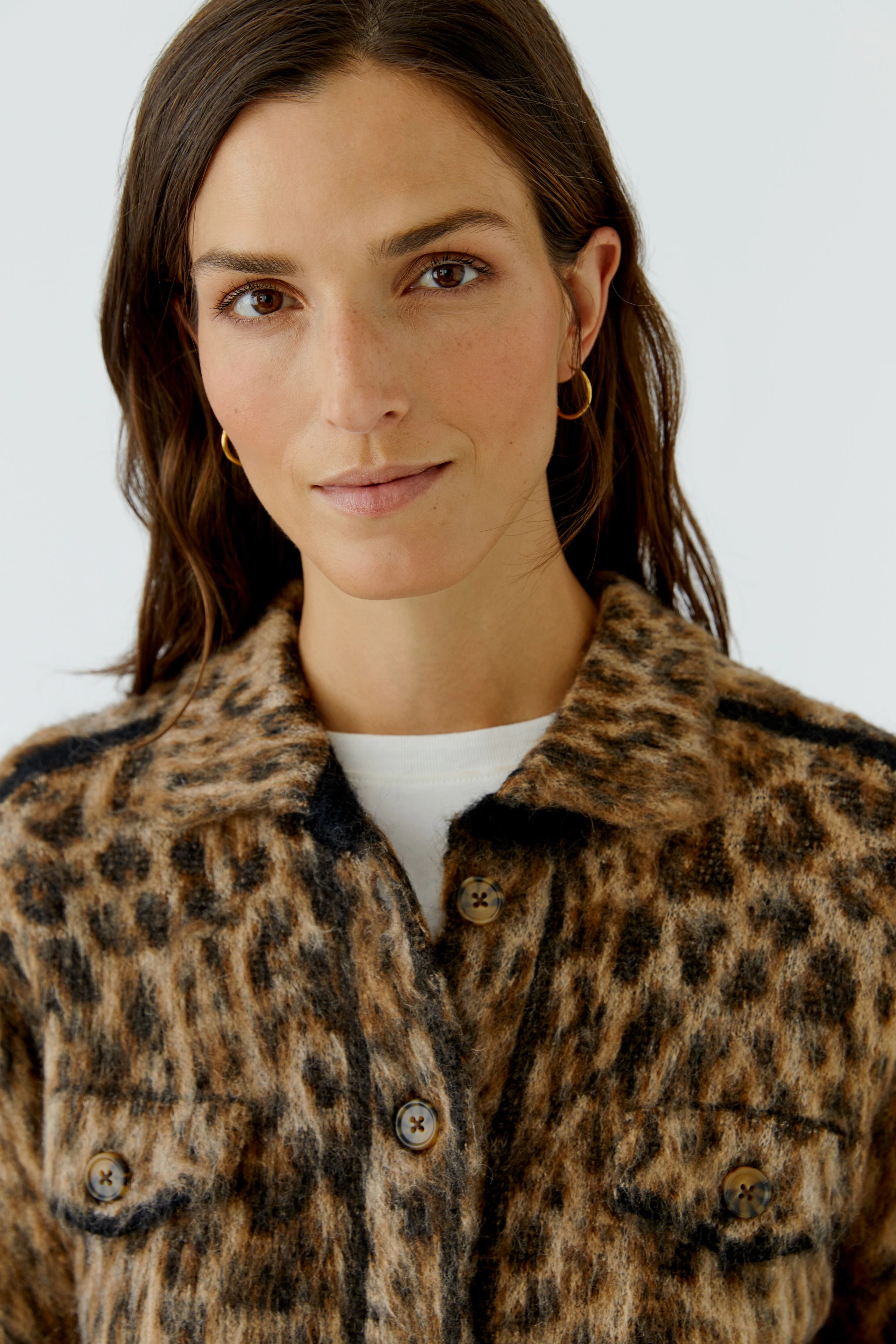 Woman in leopard print cardigan, buttoned up, with a white top underneath, looking confidently.