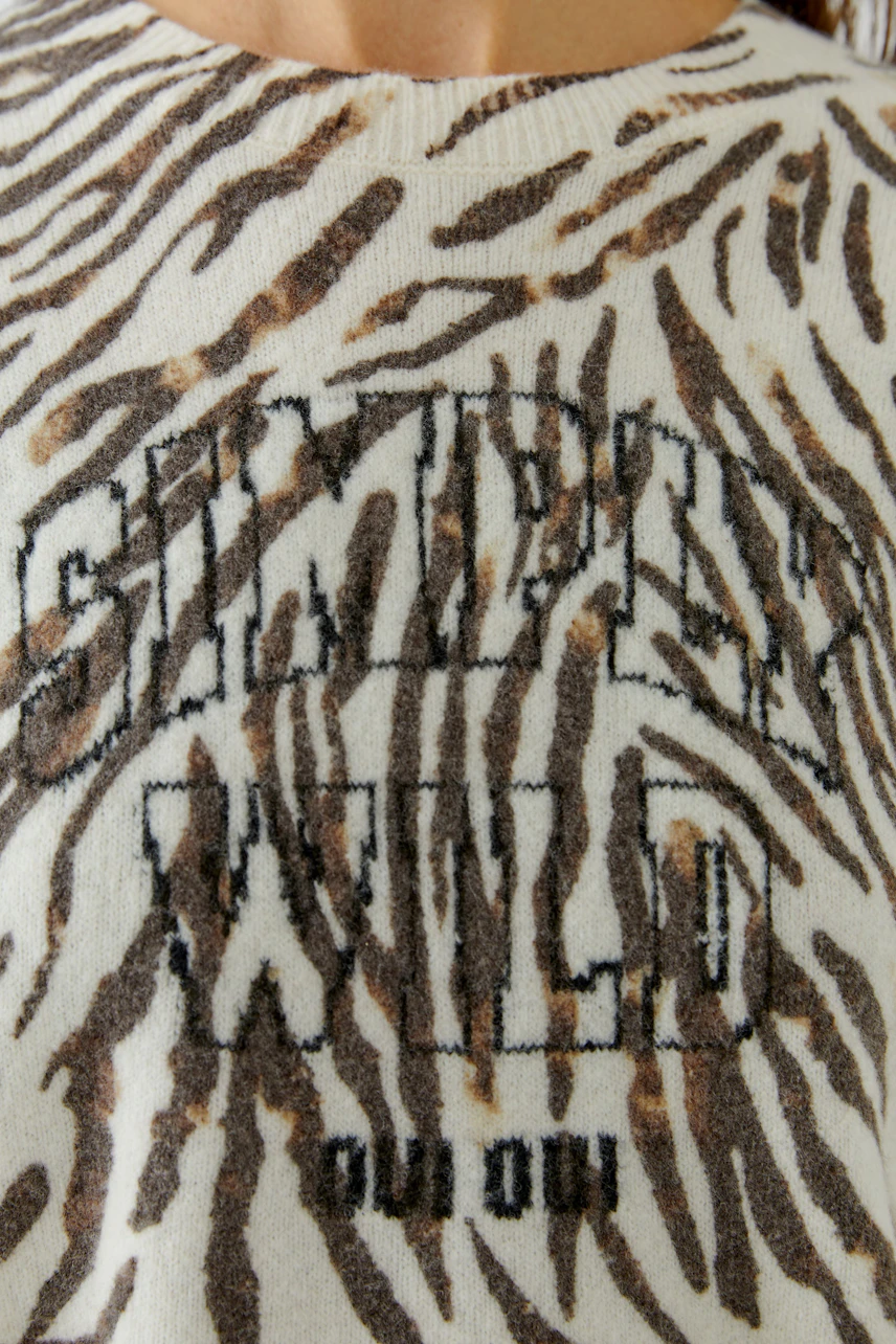 Damen-Pullover: Frau im Pullover mit wildem Muster und Schriftzug "Stay Wild".