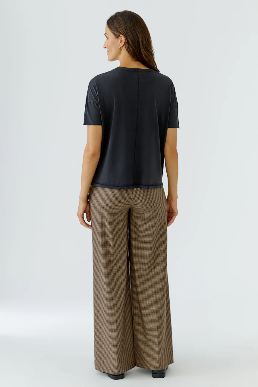 Casual women's T-shirt: Woman in a dark T-shirt and wide-leg pants, viewed from the back.