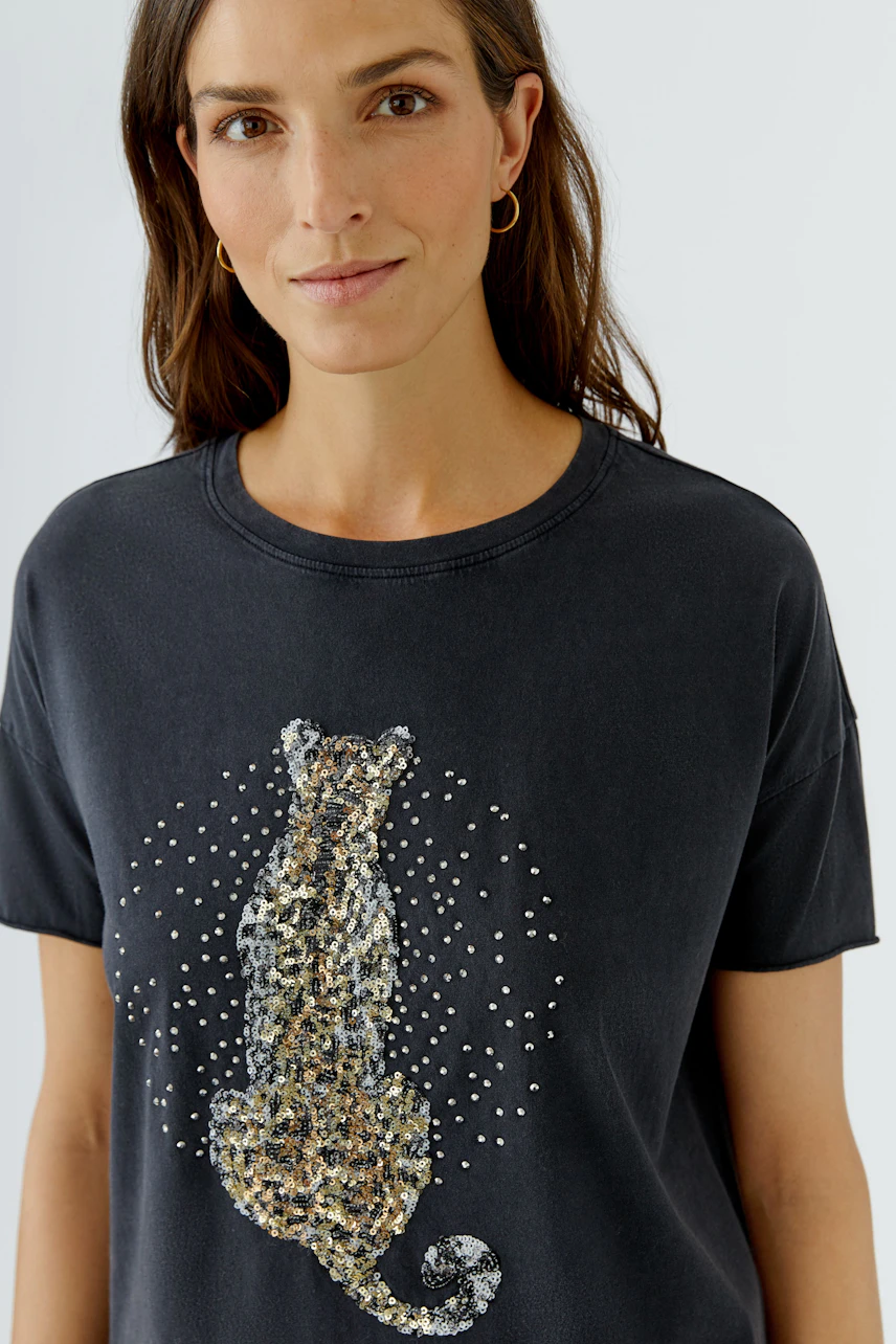 Casual women's T-shirt: Woman in a black T-shirt with a leopard print design, looking relaxed.