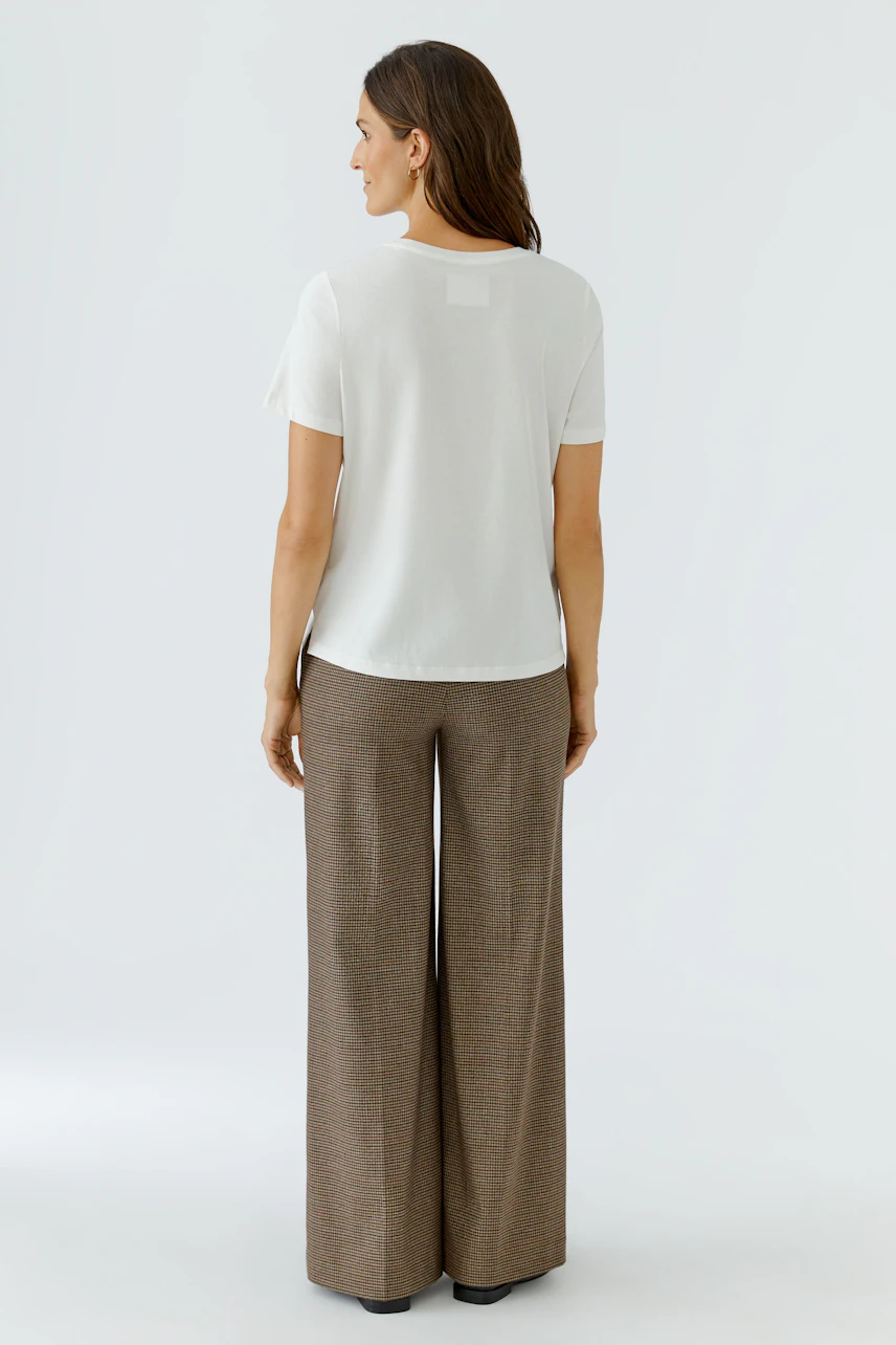 Casual women's T-shirt: Woman in a white T-shirt and brown wide-leg pants, viewed from the back.
