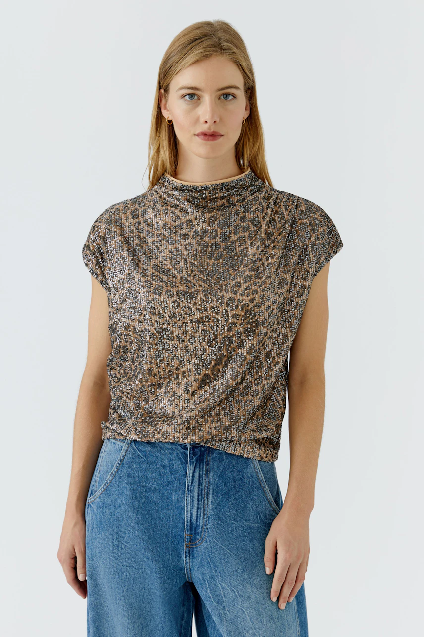 Blusenshirt: Frau im gemusterten Blusenshirt und blauer Jeans, schaut direkt in die Kamera.