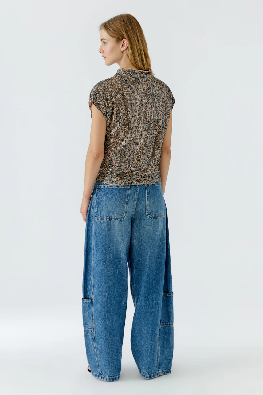 Blusenshirt: Frau im gemusterten Blusenshirt und weiten Jeans, seitlich stehend.