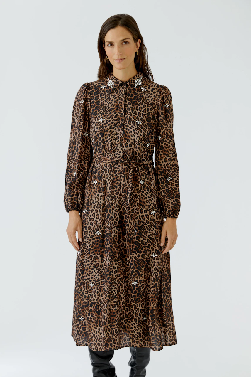 Leoparden-Muster Maxikleid: Frau im langärmeligen Kleid mit Kragen und Bindegürtel, trägt schwarze Stiefel.