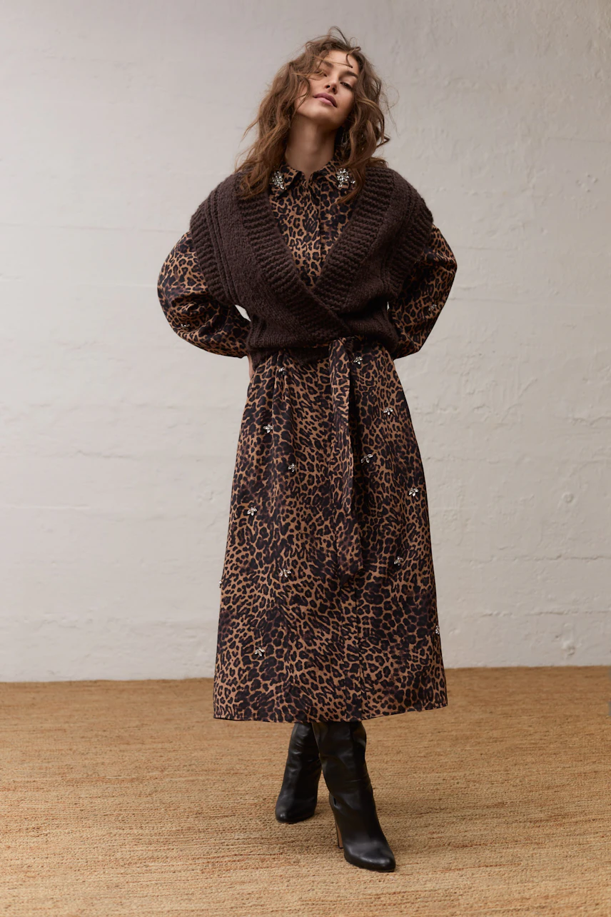 Frau im Maxikleid mit Leopardenmuster und brauner Strickweste, schwarze Stiefel, lässiger Look.