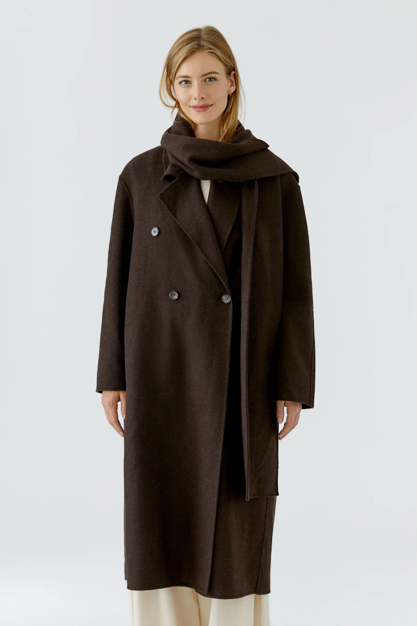Winter coat: Woman in a dark, long coat with a matching scarf, standing confidently.