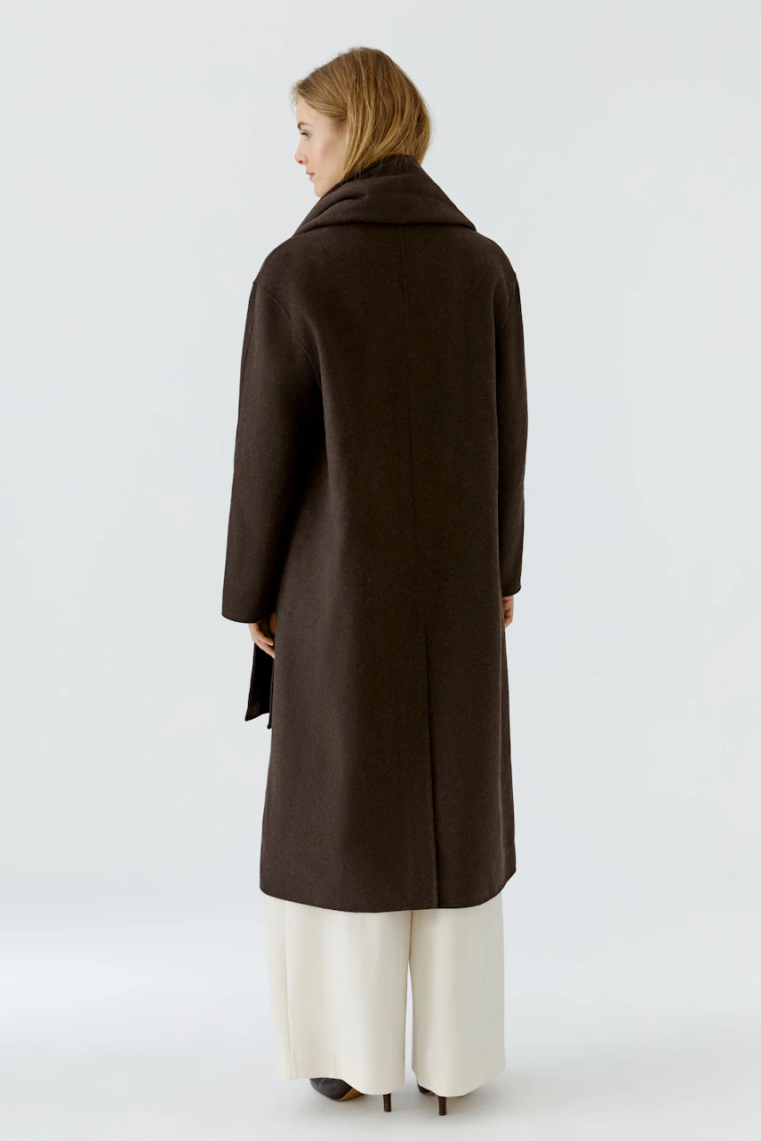 Winter coat: Woman in a long, dark coat with wide collar, standing confidently in white pants.