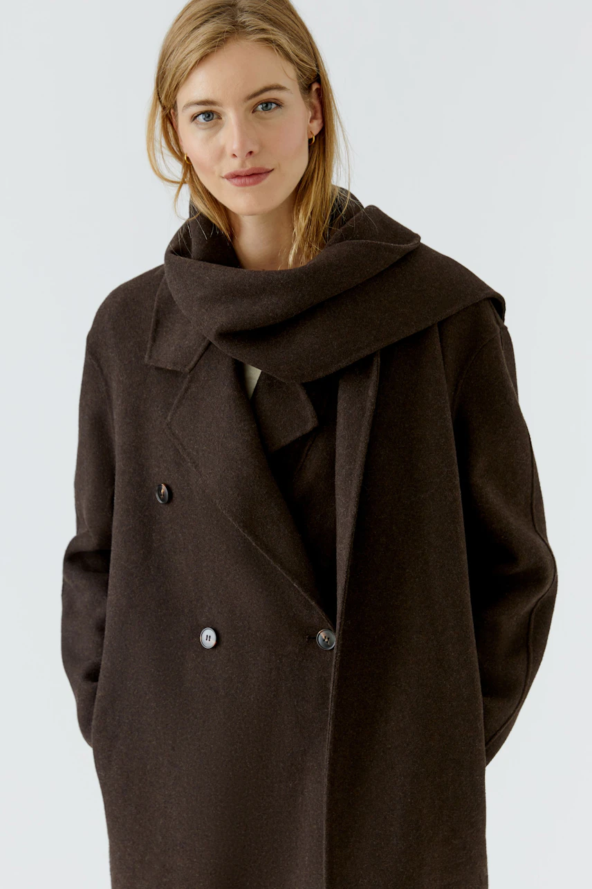 Woman in a dark winter coat with a wide collar and button details, looking confidently at the camera.