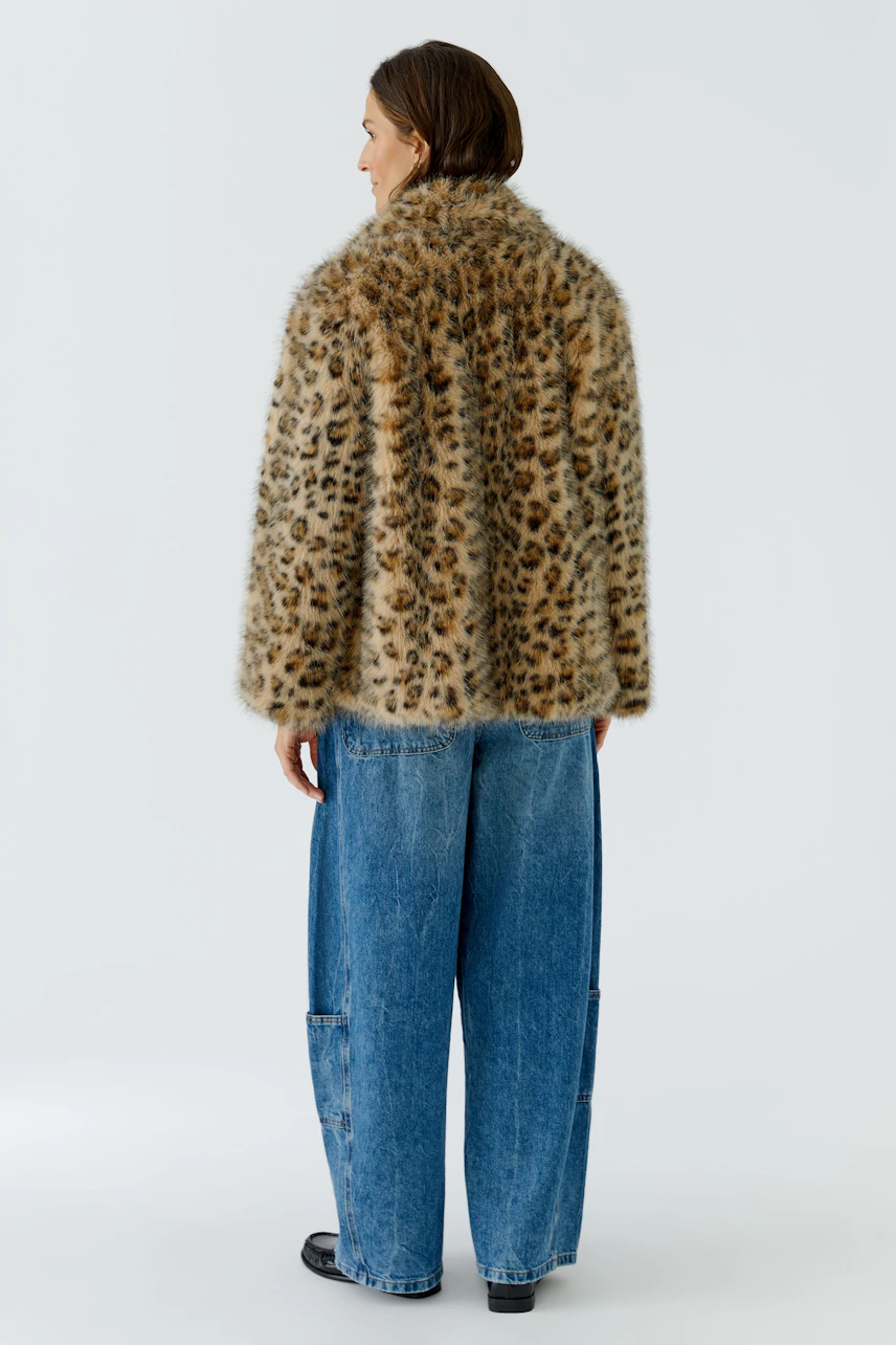 Frau in lässiger Outdoorjacke mit Leopardenmuster, kombiniert mit blauer Jeans. Rückansicht.