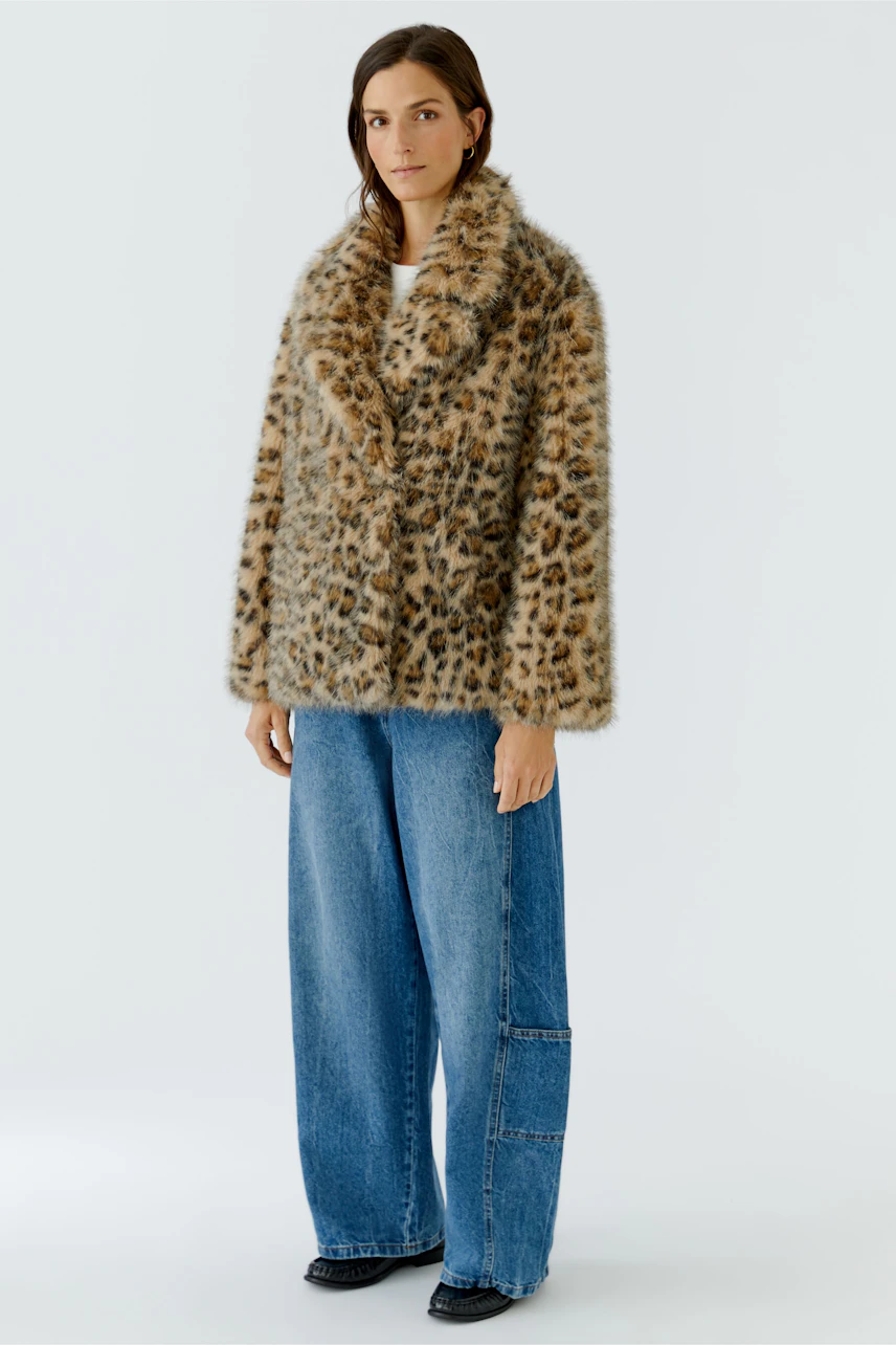 Outdoorjacke: Frau in lässiger, gemusterter Jacke mit weitem Schnitt und Jeans, schaut selbstbewusst.