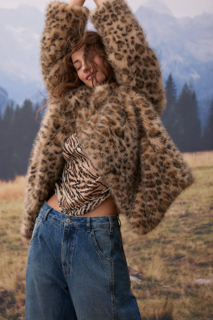Frau in lässiger Outdoorjacke mit Leopardenmuster, kombiniert mit Jeans und gestreiftem Top.