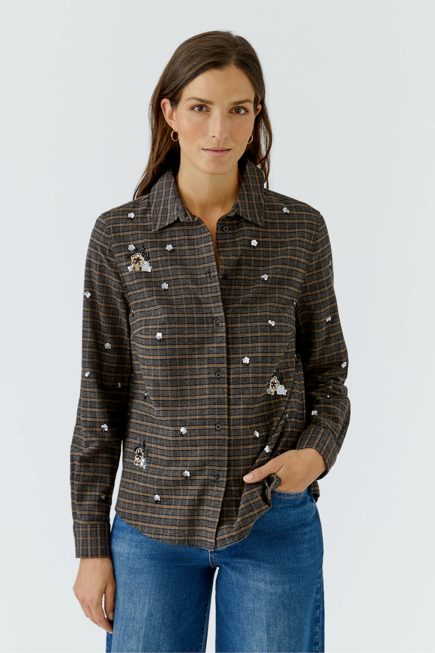 Kariertes Hemdbluse: Frau in brauner Bluse mit Blumenmuster und blauen Jeans, lässig und modern.