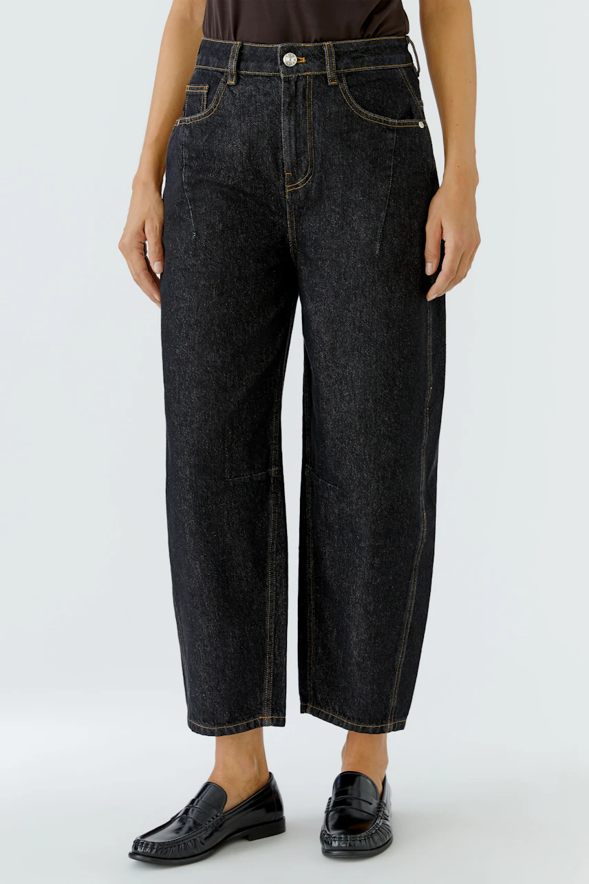 Jeans Barrel: Frau in schwarzer Barrel-Jeans, lässig geschnitten, mit braunem Oberteil und schwarzen Schuhen.