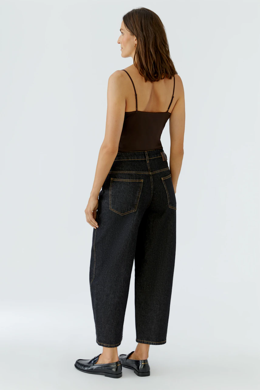 Frau in Jeans Barrel: Dunkle, weite Jeans mit hohem Bund, kombiniert mit schlichtem Top und flachen Schuhen.