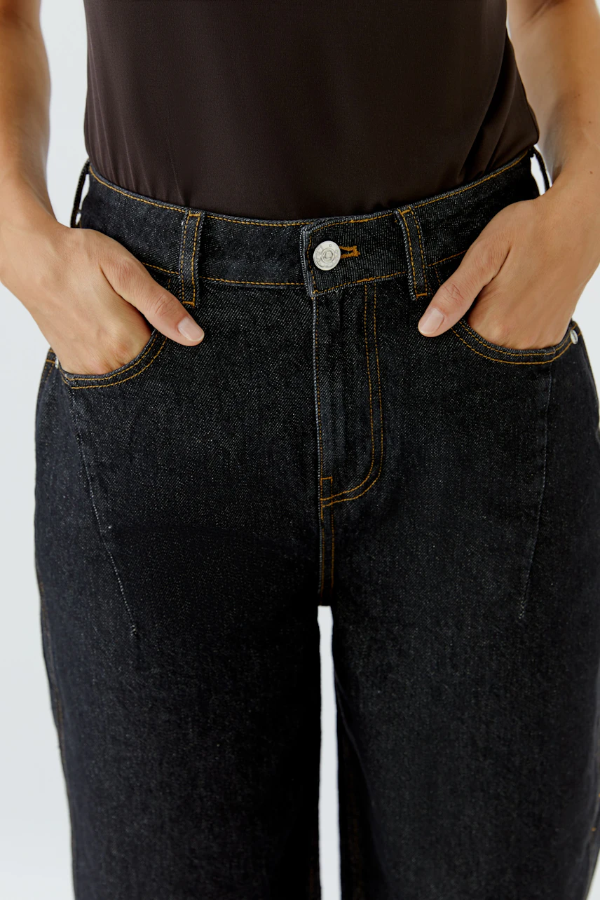 Jeans Barrel: Frau in schwarzer Barrel-Jeans, lässig und modern, mit Händen in den Taschen.