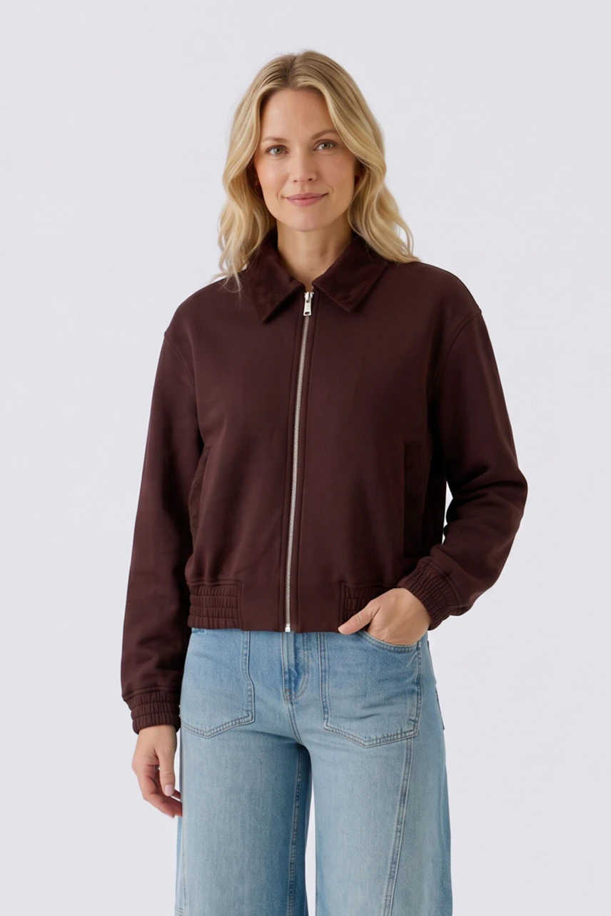 Damen-Jacke: Frau in brauner Jacke mit Reißverschluss und blauer Jeans, lässiger Look.