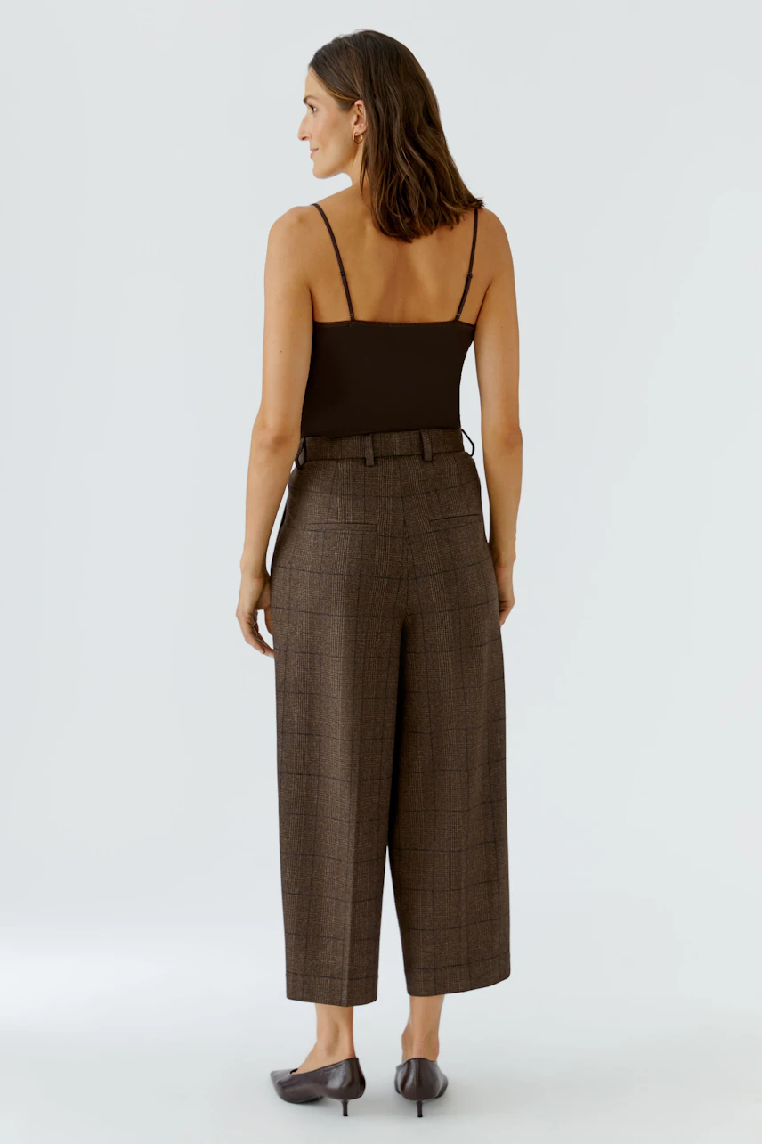 Woman in brown pleated trousers, black top, and flats, showcasing a stylish and relaxed look.