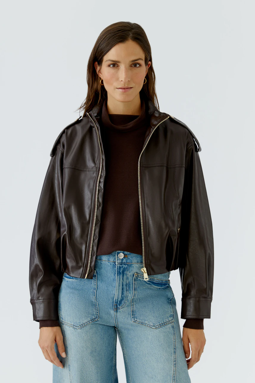 Lederimitatjacke: Frau in brauner Jacke mit Reißverschluss, kombiniert mit Jeans und dunklem Pullover.