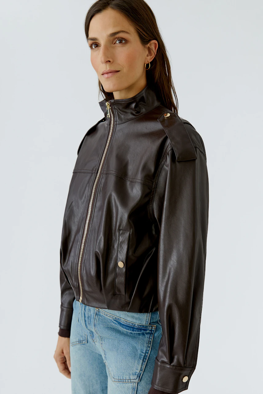 Lederimitatjacke: Frau in brauner Jacke mit Reißverschluss und Jeans, lässiger Look.