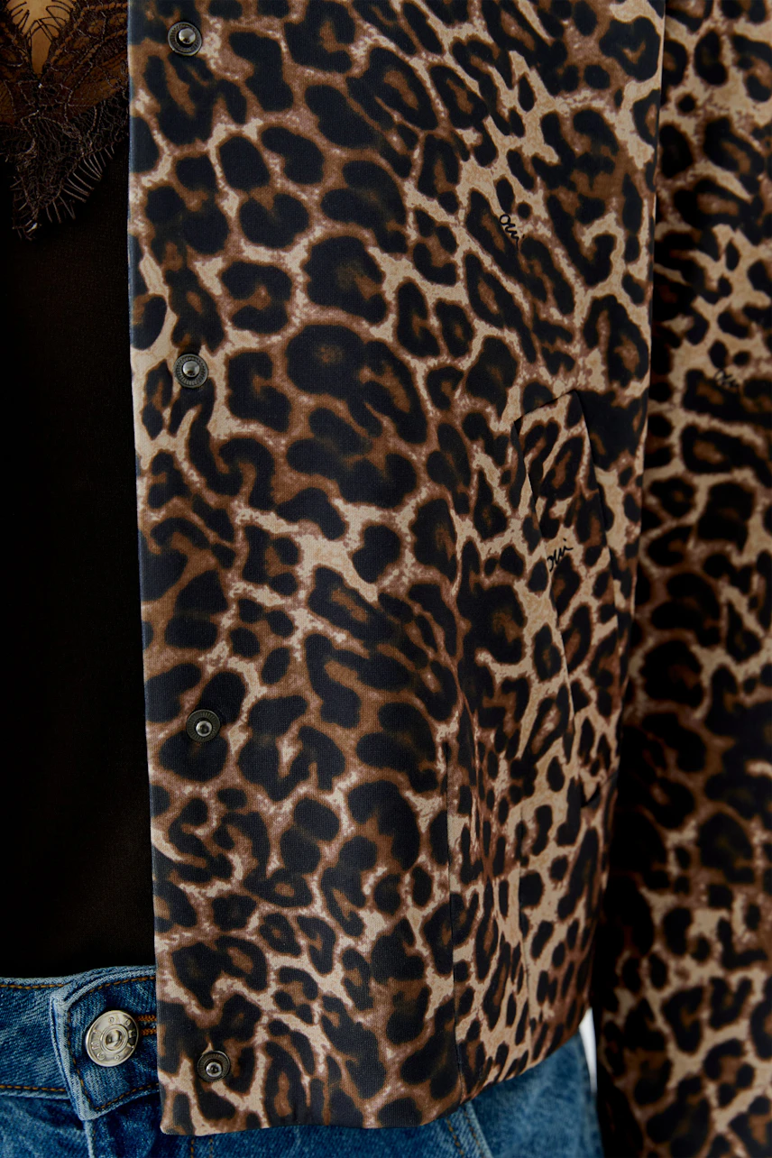 Leopardenmuster-Jacke: Frau trägt auffällige Jacke mit Leopardenmuster, kombiniert mit schwarzem Top und Jeans.